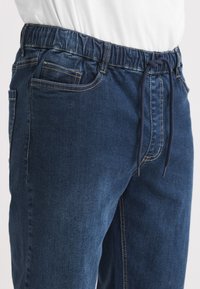 Denimjoggers i mörkblått med elastisk midja och dragsko, framfickor och kontrastsömmar längs sömmarna.