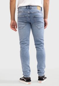 Jeans skinny de denim azul claro con un ligero desteñido, cinco bolsillos y puños elásticos, combinados con zapatillas negras y blancas.