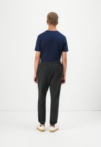 Camiseta azul marina, pantalones de chándal grises con cintura elástica y puños en los tobillos, combinados con zapatos blancos sobre un fondo simple.