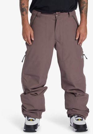 Pantalones de nieve ligeros en color malva con un corte holgado, múltiples bolsillos con cremallera y puños ajustables, combinados con zapatillas negras y blancas.
