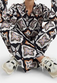 Conjunto de tela negra con patrones geométricos en blanco, púrpura y naranja; combinado con zapatillas gris claro que presentan cordones y detalles de malla.