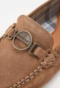 Barna velúr slip-on cipő, kerek fém Barbour logóval, varrott díszítéssel és kockás béléssel. Díszes pánttal van ellátva.