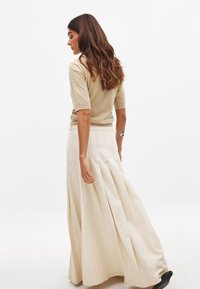 Top in maglia beige a maniche corte abbinato a una lunga gonna fluida di un leggero beige, caratterizzata da pieghe e realizzata in un tessuto testurizzato simile al lino.