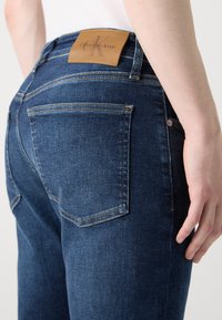 Vaqueros de mezclilla azul oscuro con una textura suave, que cuentan con una etiqueta de cuero marrón con marca en la parte trasera de la cintura y dos bolsillos traseros.