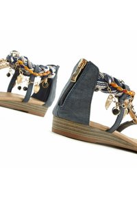 Blaue Sandalen aus Kunstleder verfügen über einen geflochtenen Textilriemen, dekorative Charms und einen seitlichen Reißverschluss für ein einfaches An- und Ausziehen. Flache Sohle mit strukturierten Details.