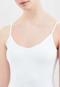 Top bianco senza maniche con spalline sottili, scollatura a forma di U e tessuto in cotone morbido e elasticizzato. Progettato per comfort e libertà di movimento.