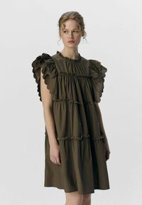 Braunes gestuftes Kleid mit Rüschensäumen und gerafften Akzenten. Glatte Textur, runder Ausschnitt, knielanges Design. Schlichte, lässige Silhouette.