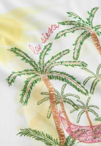 Palmeras con detalles de cuentas verdes, una hamaca rosa tejida y la frase "la siesta" bordada en rosa sobre un fondo amarillo claro.