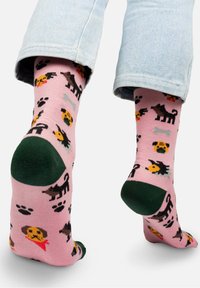 Różowe skarpetki z różnorodnymi ilustracjami psów, odciskami łap i kościami, z zielonym akcentem na pięcie. Wykonane z miękkiej, teksturowanej tkaniny.
