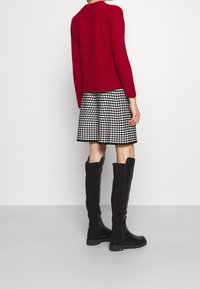 Neulottu punainen neulepaita, mustavalkoinen tikapuumallinen hame ja mustat polven korkeudella olevat nahkasaappaat. Yksinkertainen muotoilu, jossa teksturoitu neulospinta.