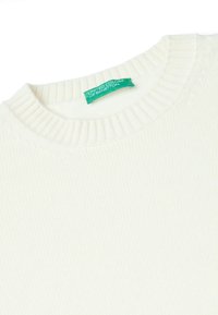 Biały sweter z prążkowanej dzianiny z okrągłym dekoltem. Na dekolcie znajduje się zielona metka z napisem "United Colors of Benetton".