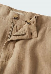 Shorts en lin beige avec fermeture par bouton, braguette zippée et poche latérale. Le tissu présente une finition texturée, améliorant sa respirabilité.