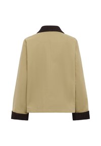 Bēšs žakets ar melnu korduroja apkakli un aprocēm. Brīvs piegriezums, gluda tekstūra un vienkārša konstrukcija. Attēlots no aizmugures.