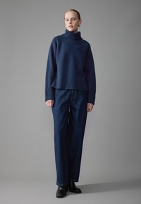 Pull col roulé bleu marine avec ourlet côtelé, associé à un jean en denim sombre à coupe ample et des bottines noires. Design simple et tissu texturé.