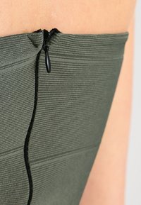 Dunkelgrünes, geripptes Stoffkleidungsstück mit einem seitlichen Reißverschluss und strukturierter Oberfläche. Minimalistisches Design, das das Reißverschlussdetail prominent zur Geltung bringt.