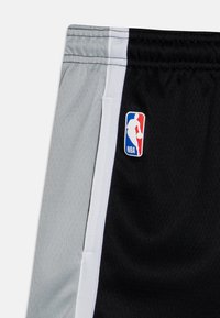 Zbliżenie czarnych i szarych spodenek do koszykówki z białymi wstawkami oraz logo NBA po czarnej stronie, blisko pasa.