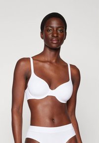 Bijeli grudnjak s žicom i tankim trakama, glatke teksture, koji ima besprijekoran dizajn i klasičan oblik, uparen s odgovarajućim bijelim donjim rubljem.