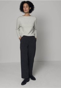 Vaaleanharmaa neule leveällä pääntiellä, yhdistettynä tummanharmaisiin leveälahkeisiin housuihin ja mustiin nilkkureihin, neutraalia taustaa vasten.