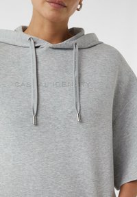 Grey oversized hoodie with a drawstring hood, featuring tonal text "CASUAL IDENTITY" on the front and metallic accents on the drawstrings.
