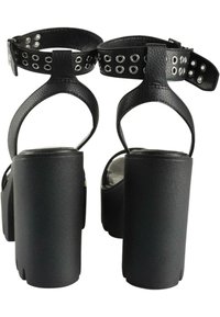 Svarta högklackade sandaler med ankelrem och ovala utskärningar, med en tjock platå och texturerad läderfinish.