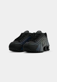 Scarpe da ginnastica nere con una tomaia texturizzata, dotate di accenti lisci in grigio e blu, e un design distintivo del tallone imbottito.
