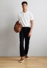 Biele polo tričko, čierne nohavice, hnedá kožená taška a hnedé topánky s bielymi podrážkami. Hladké textúry a jednoduché dizajnové prvky.