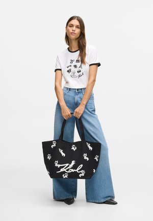 Fekete szövet bevásárlótáska, fehér macska grafikákkal és egy jól látható fehér "Karl" aláírással. A táskának dupla fogantyúja és széles nyílása van.