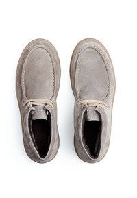 Des chaussures en suède gris avec un bout arrondi, un design à lacets, des coutures visibles et une semelle en caoutchouc lisse, vues de dessus sur un fond blanc.