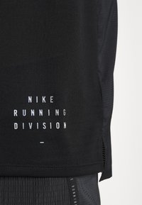 Černé sportovní tričko s texturou, bočními rozparky a bílým potištěným textem "NIKE RUNNING DIVISION" na spodní části.