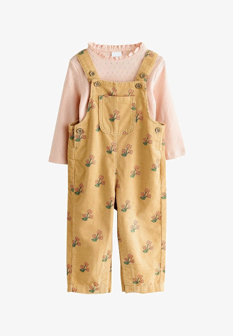 Camisa rosa de manga larga con cuello con volantes combinada con un peto amarillo de pana con pequeños estampados de flores rosas y bolsillo frontal en el pecho.