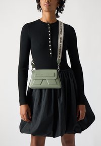 Grønn skinn crossbody-veske med geometrisk design og teksturerte detaljer, med et svart stropp med "KARL LAGERFELD"-logo.