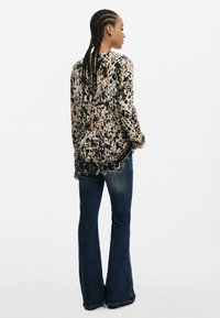 Långärmad topp med leopardmönster i lös passform, texturerat tyg och fransad nederkant. Matchas med mörka utsvängda jeans med klassisk skärning.