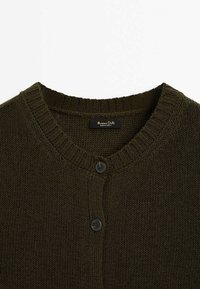 Cardigan en maille vert foncé avec encolure ronde et deux boutons noirs visibles près du col, montrant l'étiquette de la marque à l'intérieur.