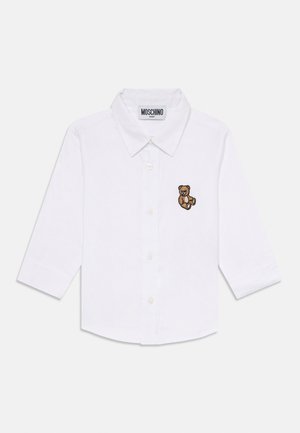 Camicia bianca per neonati con maniche lunghe, bottoni frontali, colletto, etichetta Moschino e piccolo orsetto di peluche marrone ricamato sul petto.