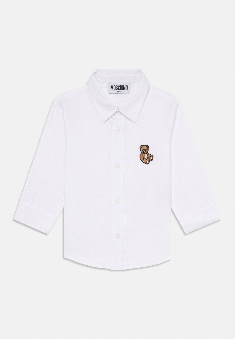 Camisa branca de bebé com mangas longas, botões frontais, colarinho, etiqueta Moschino e pequeno urso de peluche castanho bordado no peito.