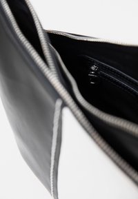 Borsa nera e bianca in pelle con chiusura a cerniera, caratterizzata da una texture liscia e cuciture a contrasto all'interno, con una piccola tasca con zip.