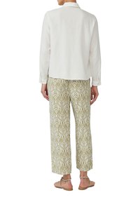 Weißes Langarmhemd mit Kragen, kombiniert mit hellgrünen gemusterten Hosen mit weißen Blättermotiven. Schlichte Sandalen runden das Outfit ab.