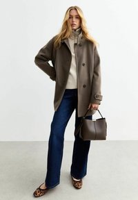 Cappotto di lana marrone con vestibilità oversize, dolcevita grigia, pantaloni a zampa d'elefante in denim scuro, ballerine leopardate e una piccola borsetta marrone.