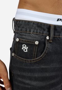 Zwarte spijkerbroek van denim met oranje stiksels, voorzien van een klein geborduurd logo op de achterzak en zilverkleurige hardware accenten.