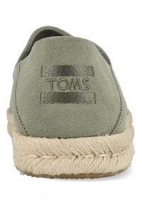 Green suede slip-on shoe with a woven jute sole, featuring a stitched TOMS logo on the upper and a rounded toe design.