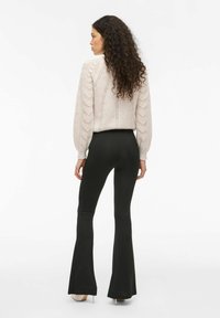 Suéter de punto rosa claro con patrón texturizado en chevron, combinado con pantalones acampanados negros y tacones beige, visto desde atrás.