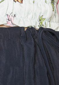 Top leve floral, de tom verde claro, com costeado em babados e calças azul-marinho de tecido suave com cordão, mostrando tecido franzido na cintura.