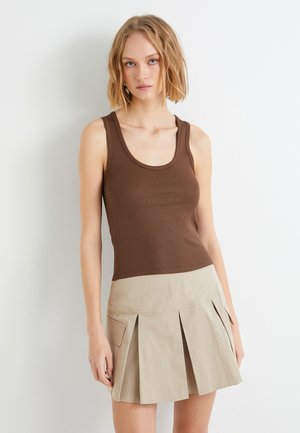 Top sin mangas de color marrón ribeteado combinado con una falda corta plisada de color beige con bolsillos laterales y una textura suave. Diseño simple y ajustado.