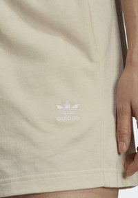 Ljust beige bomullsshorts med en broderad vit Adidas-logga. Slät textur med rak passform och sidoseamsdetaljer.