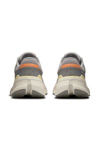 Zapatillas grises con acentos en naranja y amarillo, que cuentan con una parte superior de malla texturizada y una suela robusta y acolchada con un dibujo en relieve.
