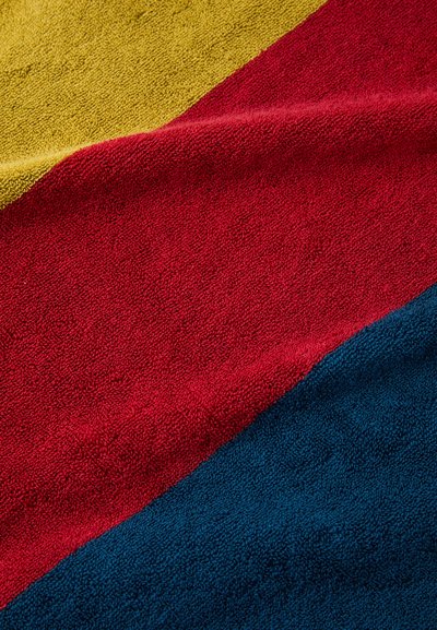 Cotton towel featuring a zigzag pattern in yellow, red, and blue sections. The texture is soft with a plush, absorbent surface.