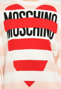 Pullover lavorato a maglia con strisce orizzontali rosse e bianche, grande cuore rosso e logo "Moschino" nero in bold al centro.