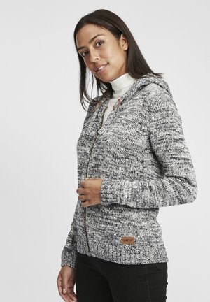 Hoodie en tricot gris et blanc avec fermeture éclair à l'avant, deux accents en cuir marron, et poignets côtelés. Étiquette de marque visible en bas à gauche.