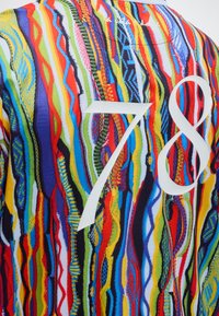 Φωτεινό πολύχρωμο πλεκτό ύφασμα με κάθετες κυματιστές ρίγες σε κόκκινο, μπλε, κίτρινο, πράσινο και μαύρο, με μεγάλα λευκά νούμερα "78" στην κορυφή.