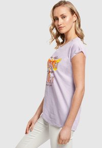 Lilac cotton t-shirt featuring short sleeves, round neckline, and a colorful graphic print. Smooth texture, casual design, worn with white pants.
